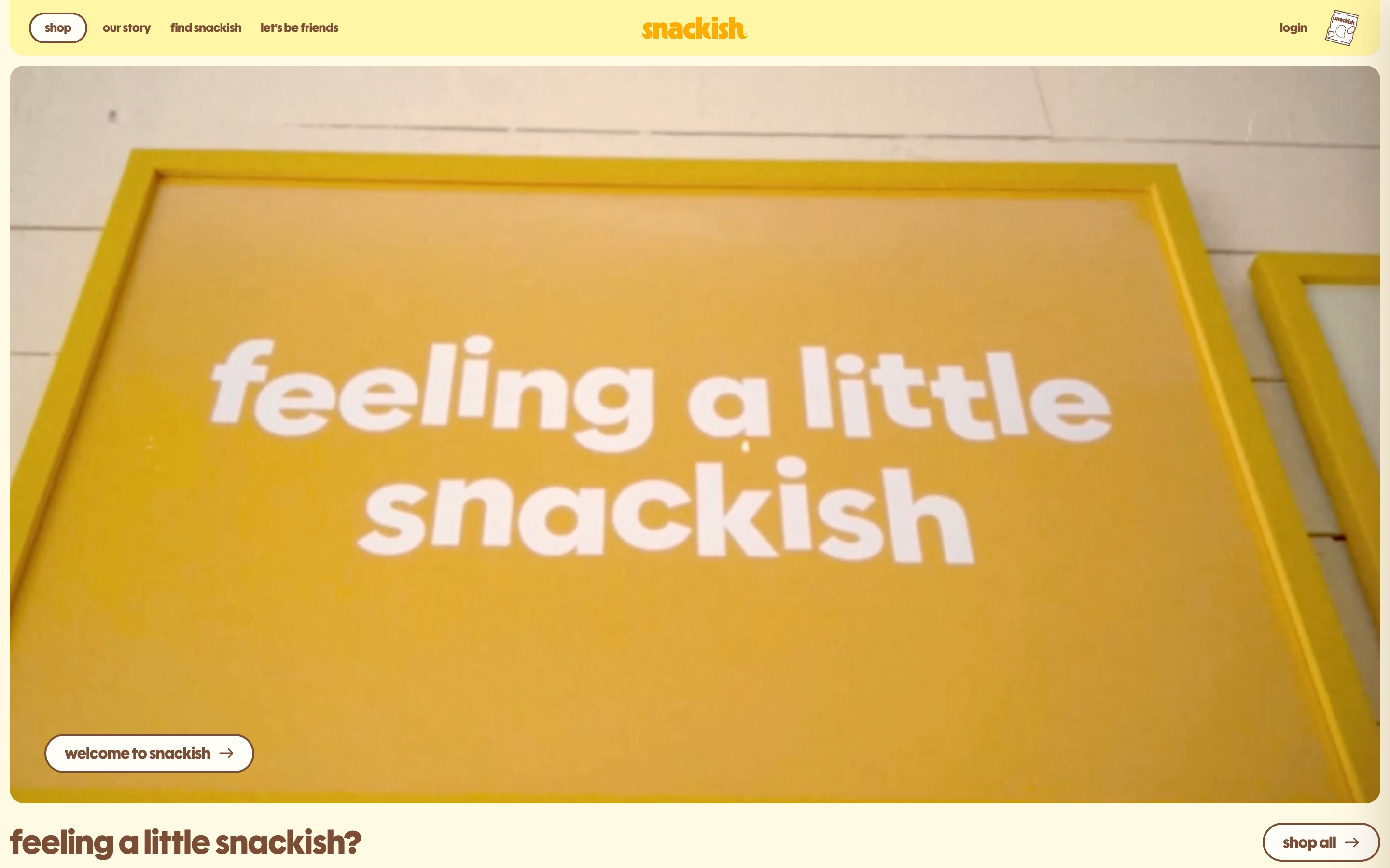 Snackish hero: pale yellow nav, photo of a yellow framed sign saying feeling a little snackish, welcome and shop all buttons