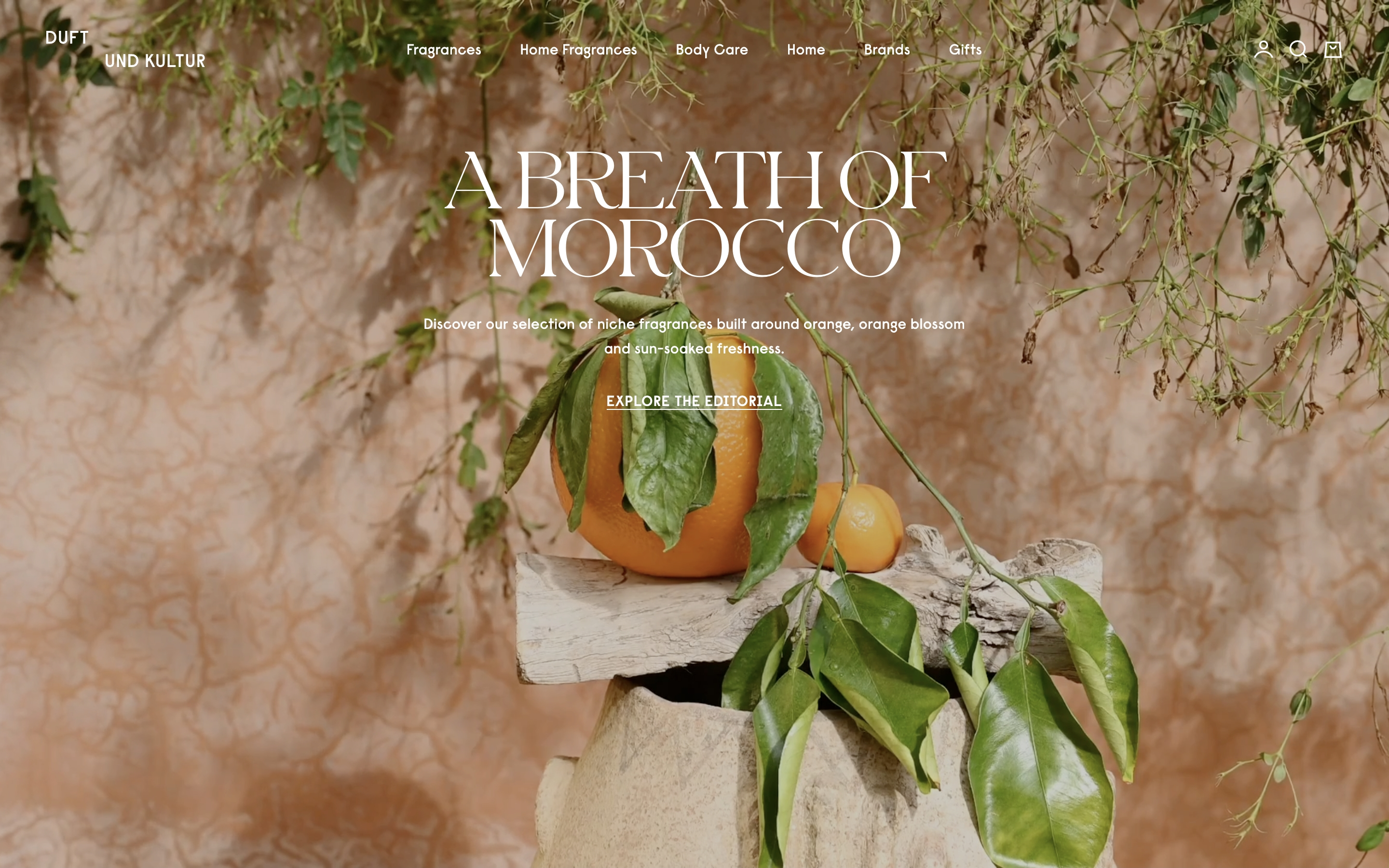 Duft und Kultur hero with oranges on wood, hanging greenery, and centered A Breath of Morocco headline.