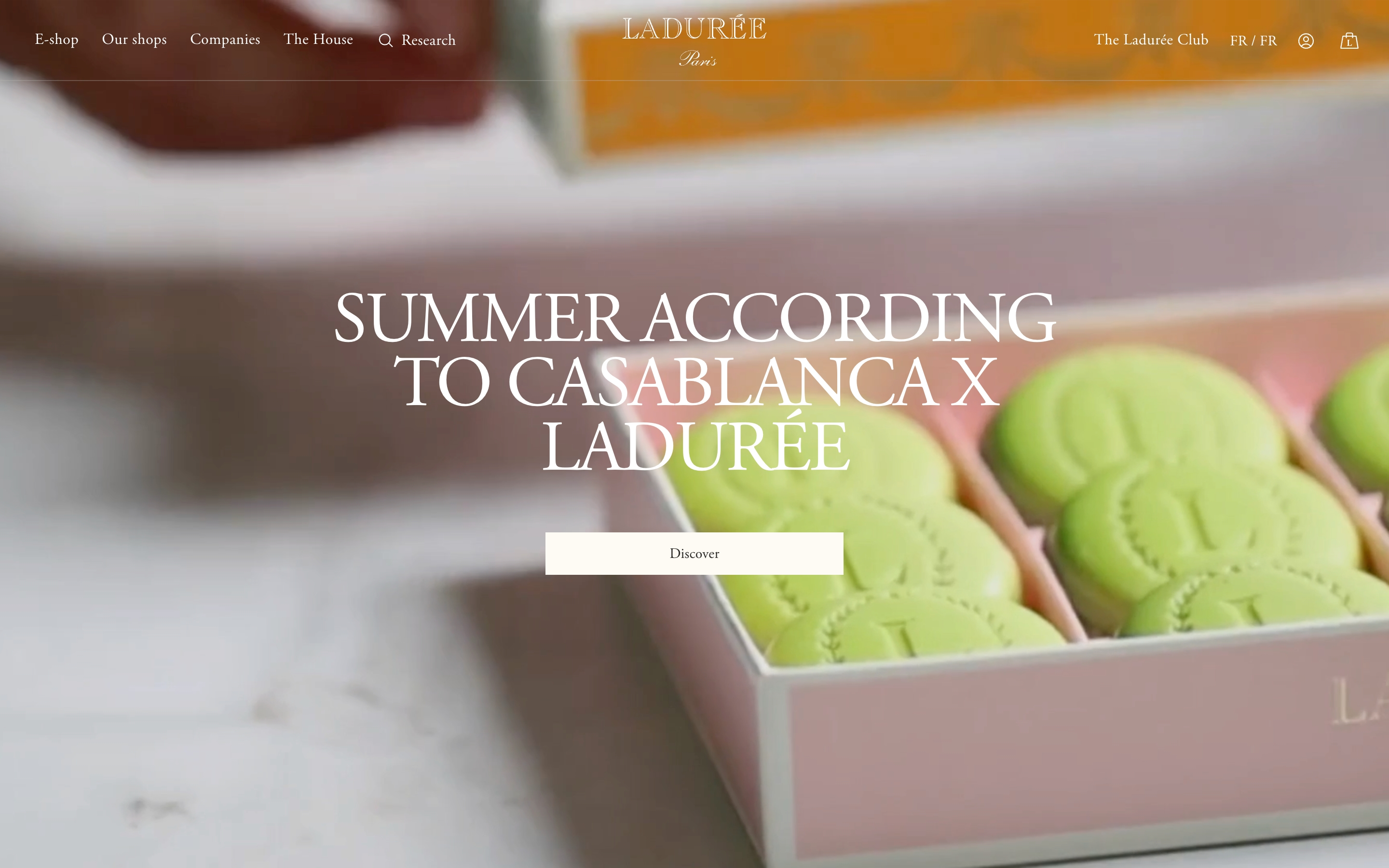 Ladurée homepage hero with oversized serif headline over mint macarons in a pink box and a Discover button
